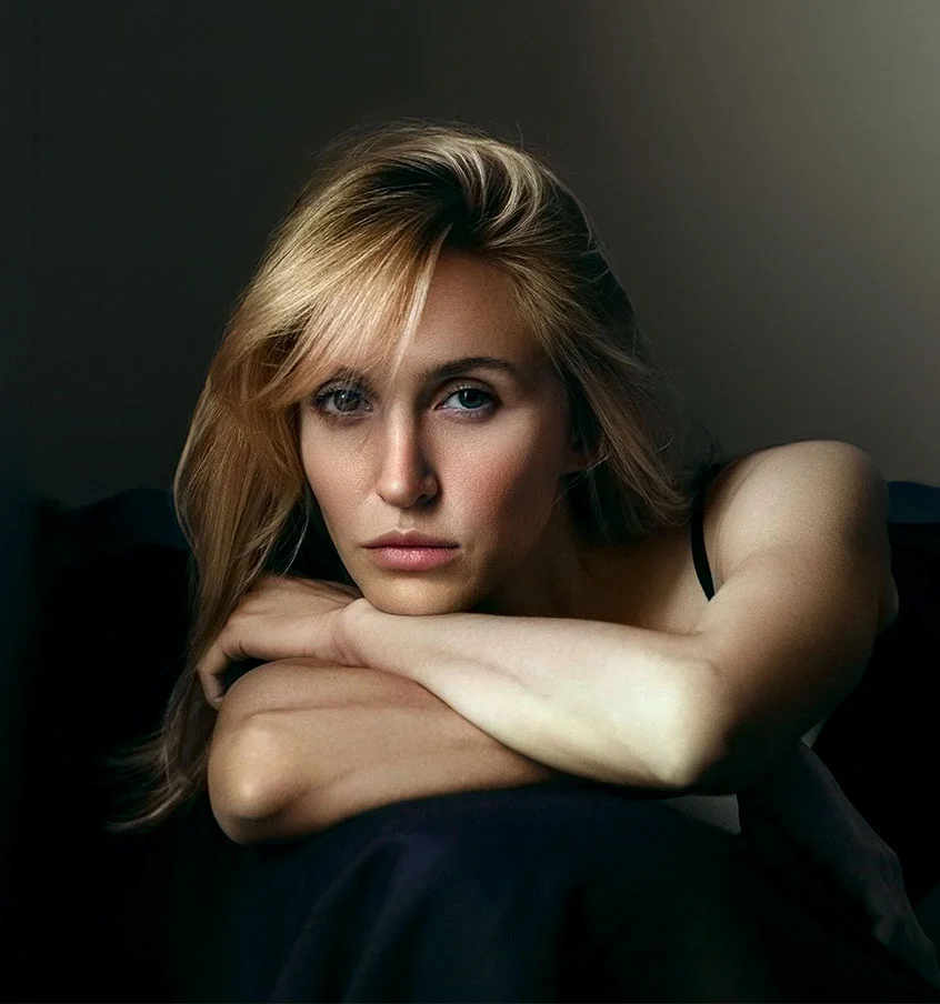 Blonde woman sitting on a couch, leaning her head on her crossed arms - Dermal Fillers in New York, NY